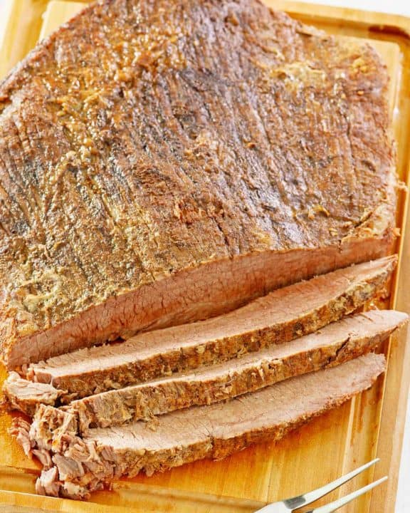 oven baked brisket and a meat fork on a cutting board