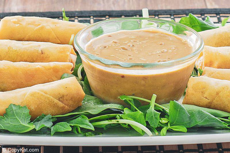 a bowl of Thai peanut sauce, spring rolls, and arugula on a platter
