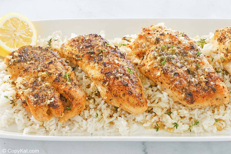 baked lemon pepper chicken on top of rice on a white platter.