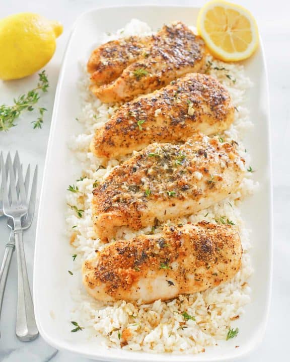 baked lemon pepper chicken with garlic over rice on a platter