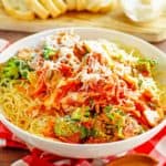 a bowl of capellini primavera and bread slices on a wood board