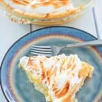 lemon meringue pie slice on a plate next to the pie