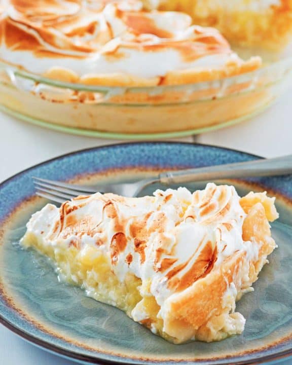 a slice of lemon meringue pie on a plate with the pie behind it