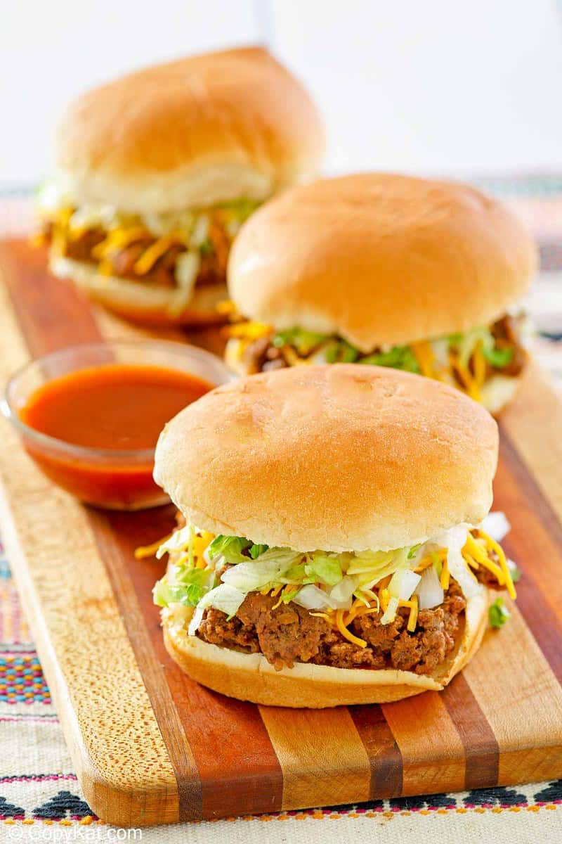 three homemade Taco Bell Bell Beefer sandwiches and taco sauce on a wood board