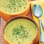two bowls of acorn squash soup, a bowl of pumpkin seeds, and two spoons.