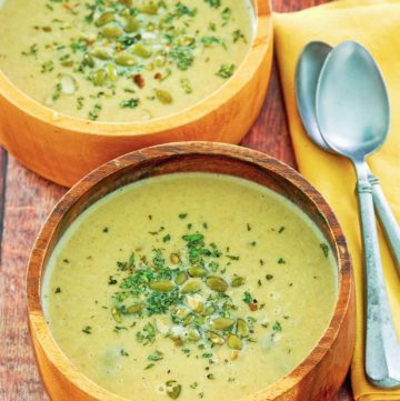 two bowls of acorn squash soup, a bowl of pumpkin seeds, and two spoons.