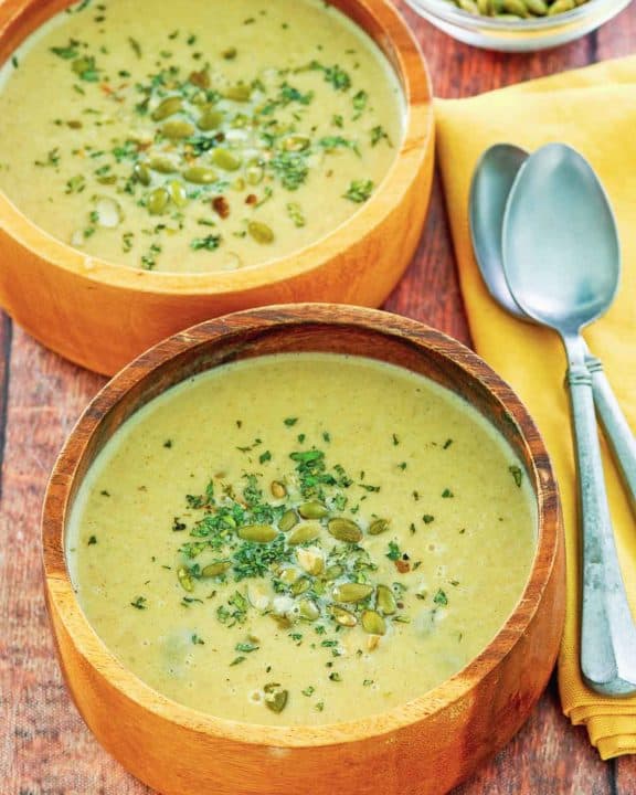 two bowls of acorn squash soup, a bowl of pumpkin seeds, and two spoons.