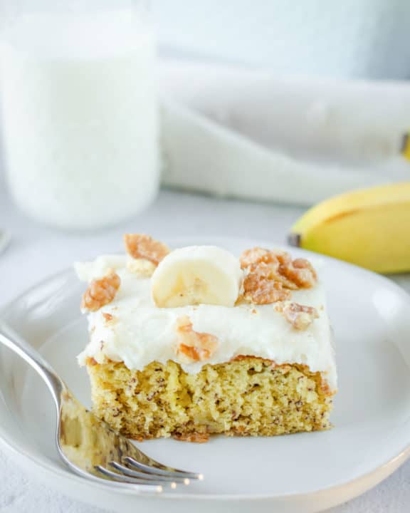 banana cake slice and a fork on a plate and a glass of milk.
