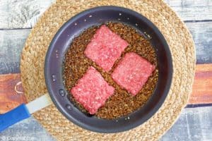 ground beef patties and onions in a skillet.
