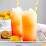 two glasses of homemade McDonald's frozen strawberry lemonade drinks and lemons on a tray.