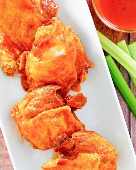 four homemade Wingstop Buffalo chicken thighs, Buffalo sauce, and celery sticks.