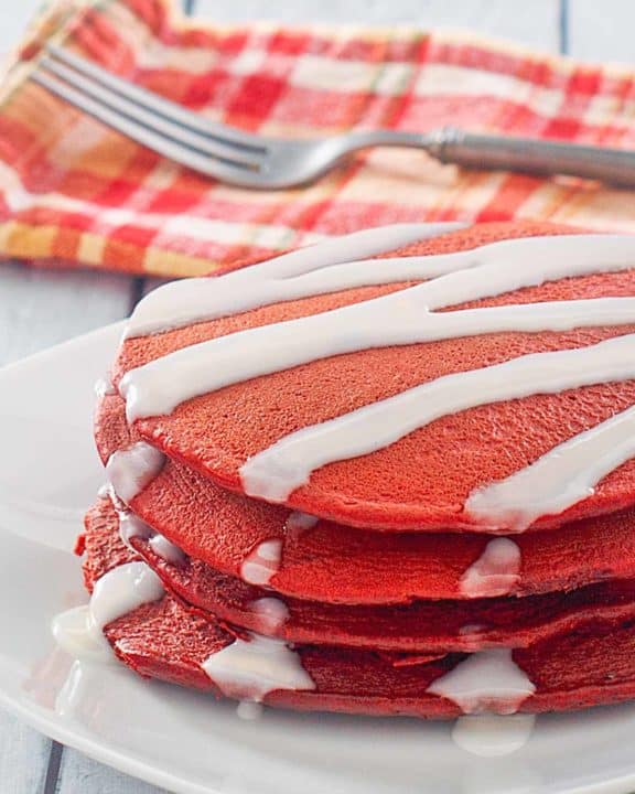 red velvet pancakes with cream cheese glaze on a plate.