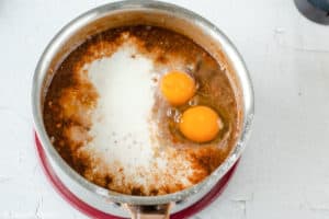 adding eggs, buttermilk, and vanilla to chocolate cake batter mixture in a saucepan.
