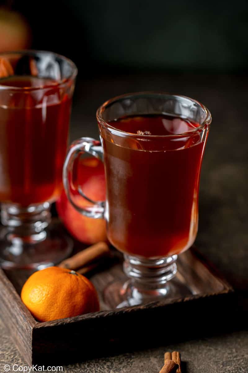 wassail in two mugs, an orange, and cinnamon sticks.
