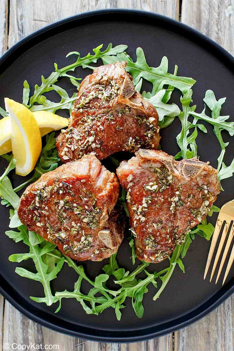 overhead view of pan seared lamb chops, arugula, and lemon wedges on a plate.