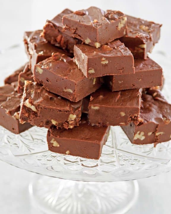 homemade See's chocolate fudge with nuts on a cake stand.