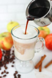 pouring espresso into frothed milk in a mug.