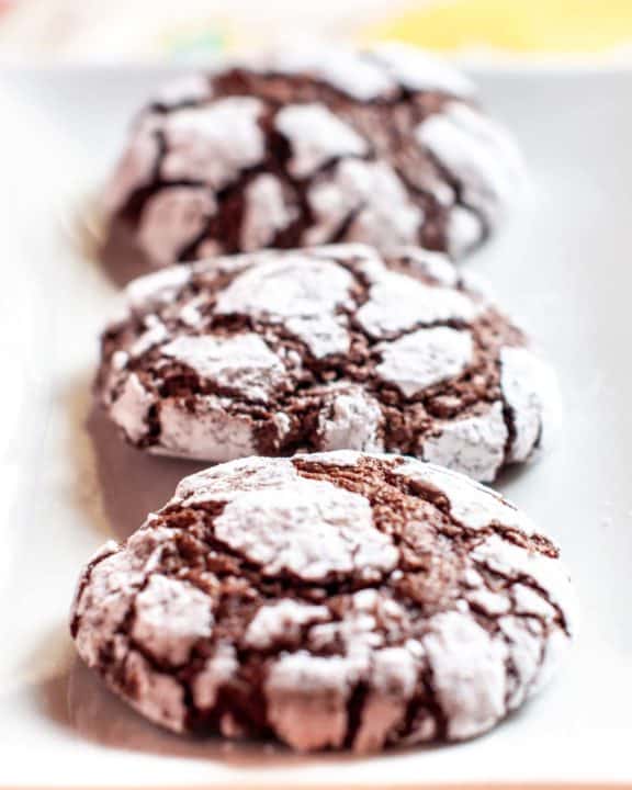 three chocolate crinkle cookies on a plate.