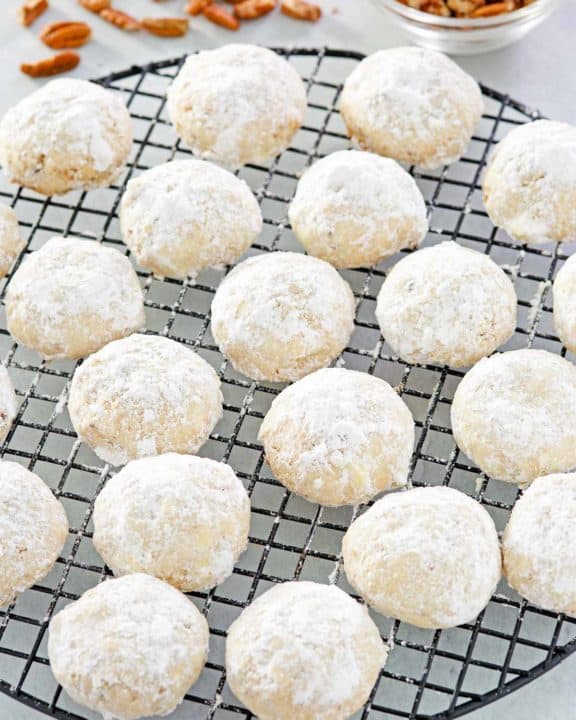 pecan sandies cookies on a round wire rack and a bowl of pecans.