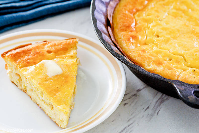 sour cream cornbread slice on a plate next to the cornbread in a skillet.
