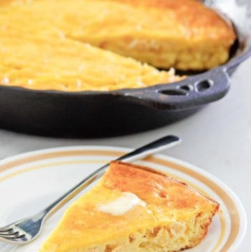 sour cream cornbread slice on a plate in front of cornbread in a skillet.