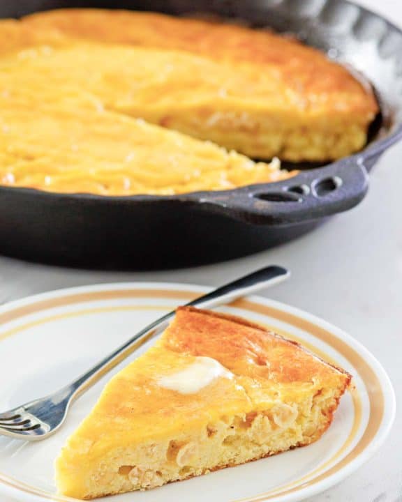 sour cream cornbread slice on a plate in front of cornbread in a skillet.