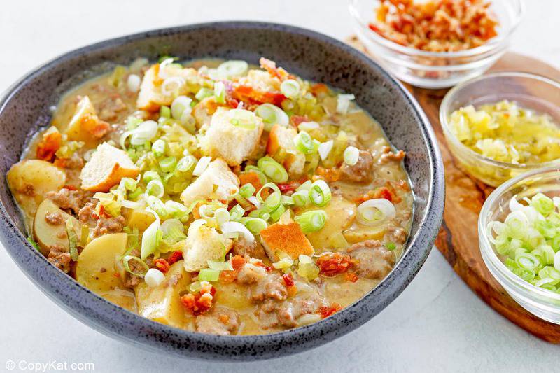 a bowl of cheeseburger soup with toppings in bowls beside it.