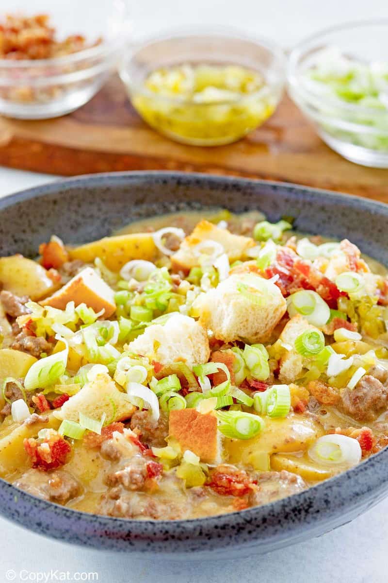 bowl of cheeseburger soup with toppings in bowls behind it.