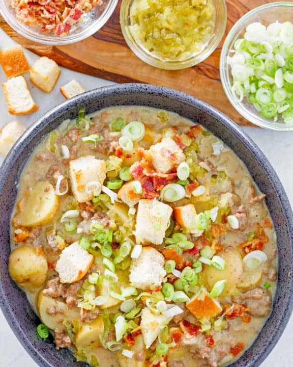 overhead view of cheeseburger soup in a bowl and various toppings for it.