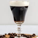Irish coffee on a wood board with coffee beans around it.