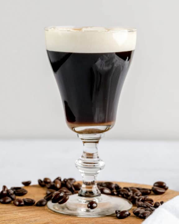 Irish coffee on a wood board with coffee beans around it.