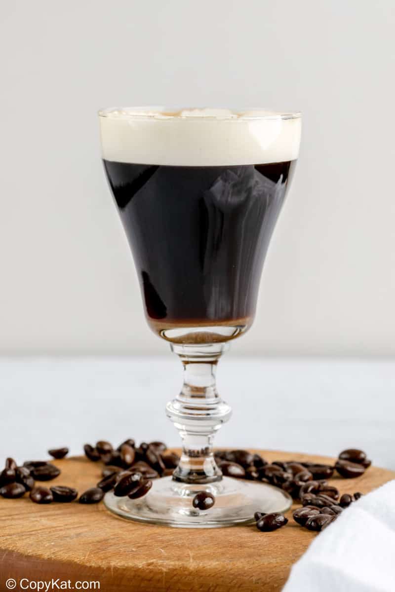 Irish coffee on a wood board with coffee beans around it.