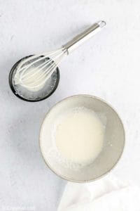 slightly whipped cream in a bowl and a whisk.