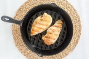 two cooked chicken breasts in a cast iron skillet.