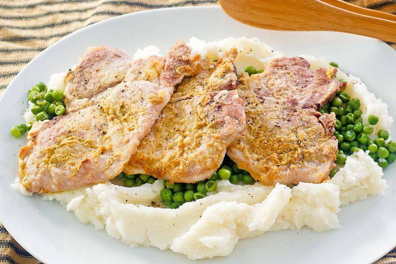mustard pork chops, peas, and mashed potatoes on a white platter.