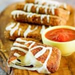 homemade Olive Garden fried mozzarella sticks and a cup of marinara sauce on a wood board.