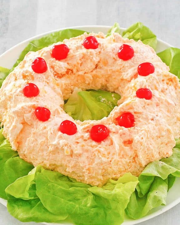 orange fluff jello salad on top of lettuce on a platter.