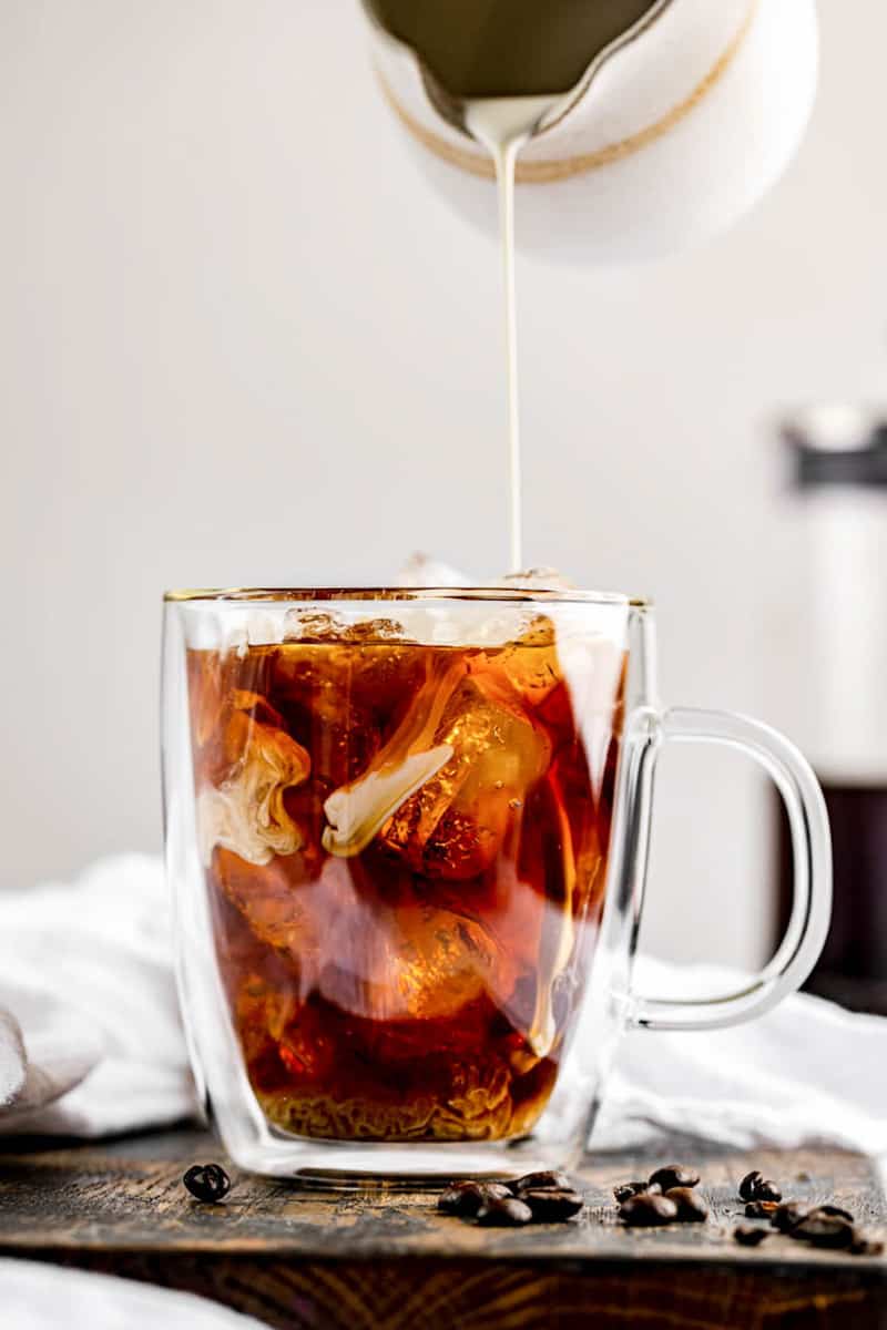 pouring cream into a cup of cold brew coffee.