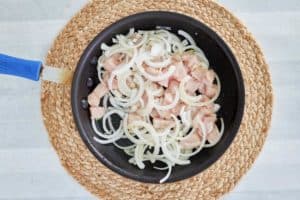 chicken pieces and onion slices in a skillet.