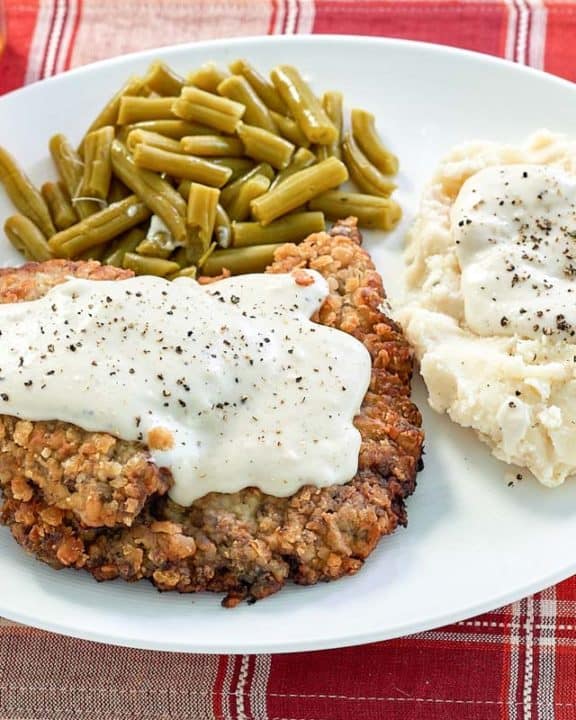 copycat Cracker Barrel country fried steak, sides, and gravy on a plate.