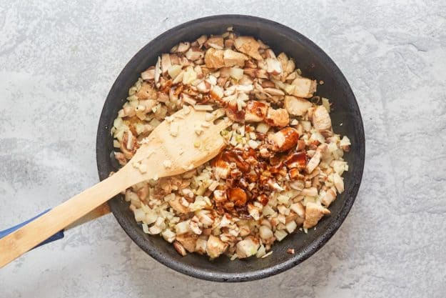 adding sauce to chicken lettuce wraps filling in a skillet.