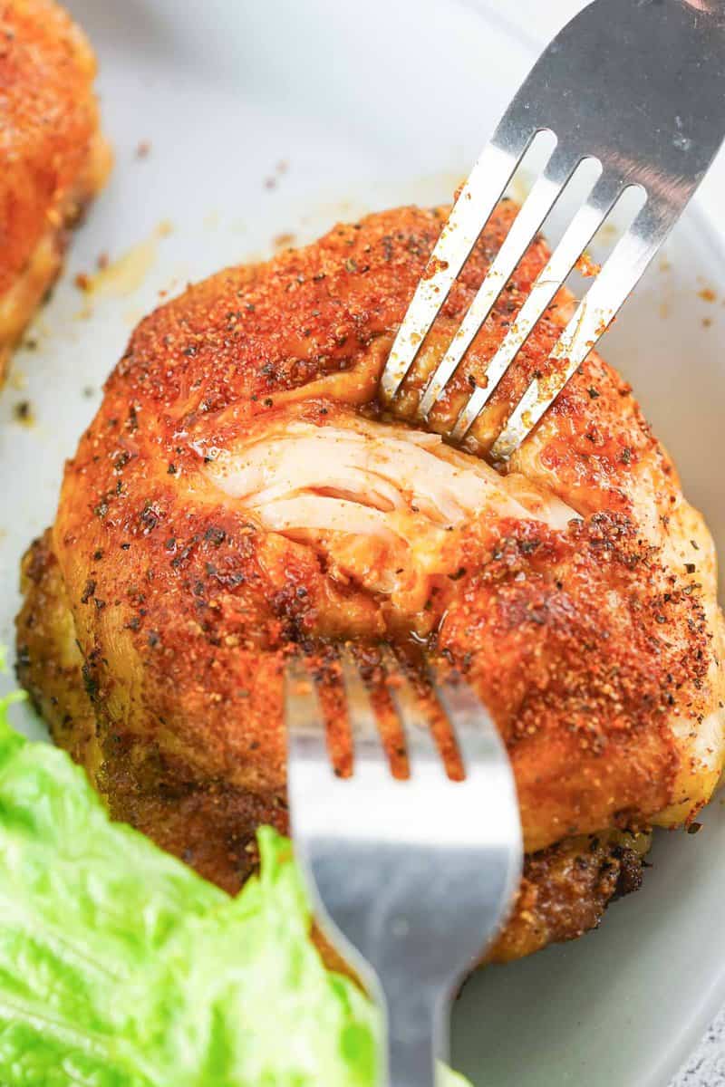 two forks pulling apart a smoked chicken thigh.