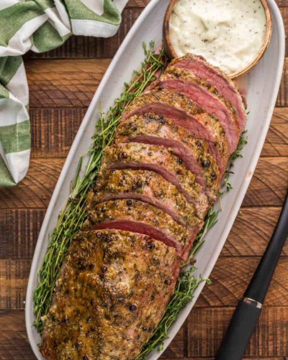 overhead view of smoked eye of round roast and horseradish sauce on a platter.