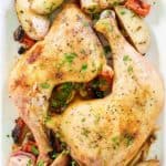 overhead view of baked chicken leg quarters and vegetables on a white platter.