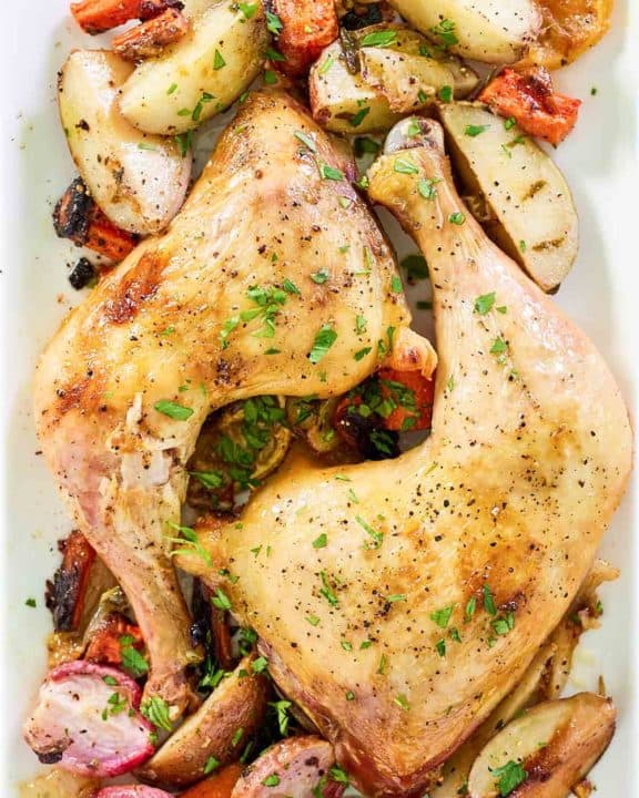 overhead view of baked chicken leg quarters and vegetables on a white platter.