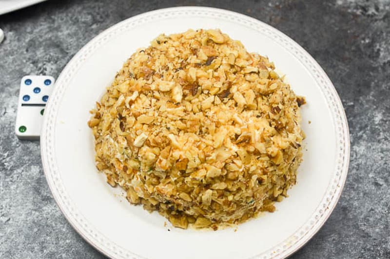 cream cheese cheese ball covered in nuts on a white plate.