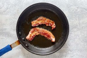 two pieces of cooked bacon in a skillet.