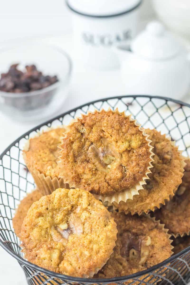 homemade oatmeal raisin muffins in a basket and a small bowl of raisins.