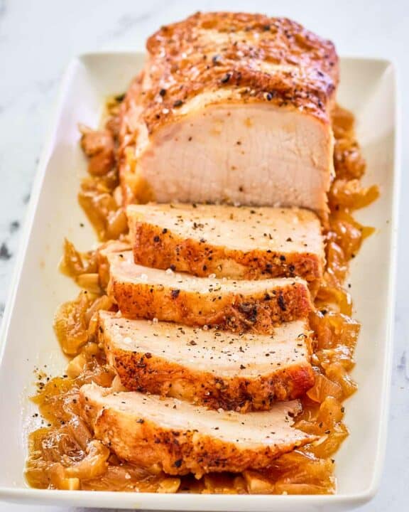 Instant Pot pork loin on top of cooked onions on a platter.