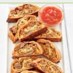 homemade sausage roll slices and a bowl of picante sauce on a platter.